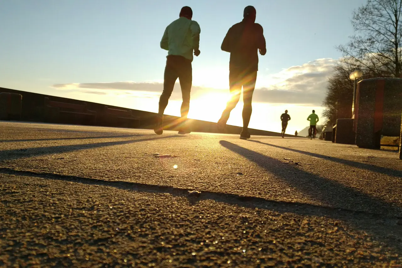 Two backlit runners on a seaside promenade