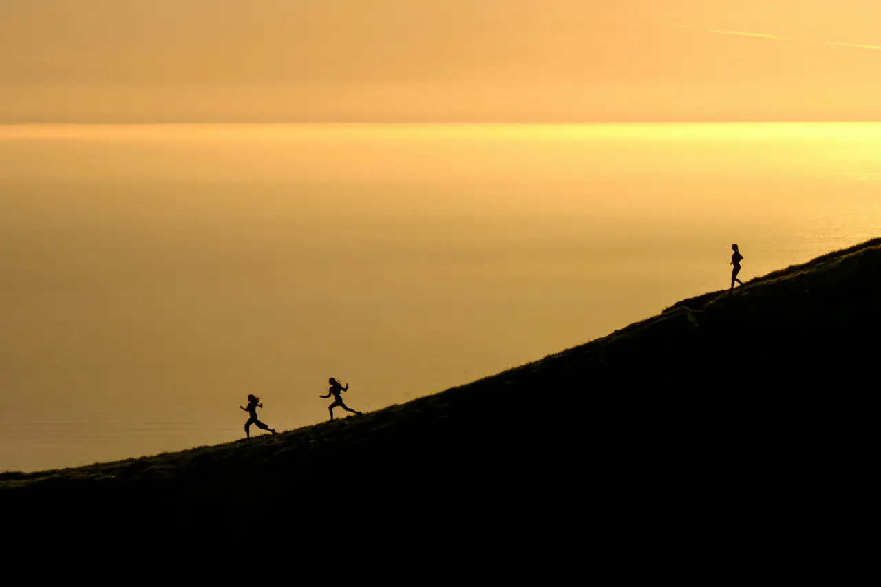 Three people running downhill above the sea