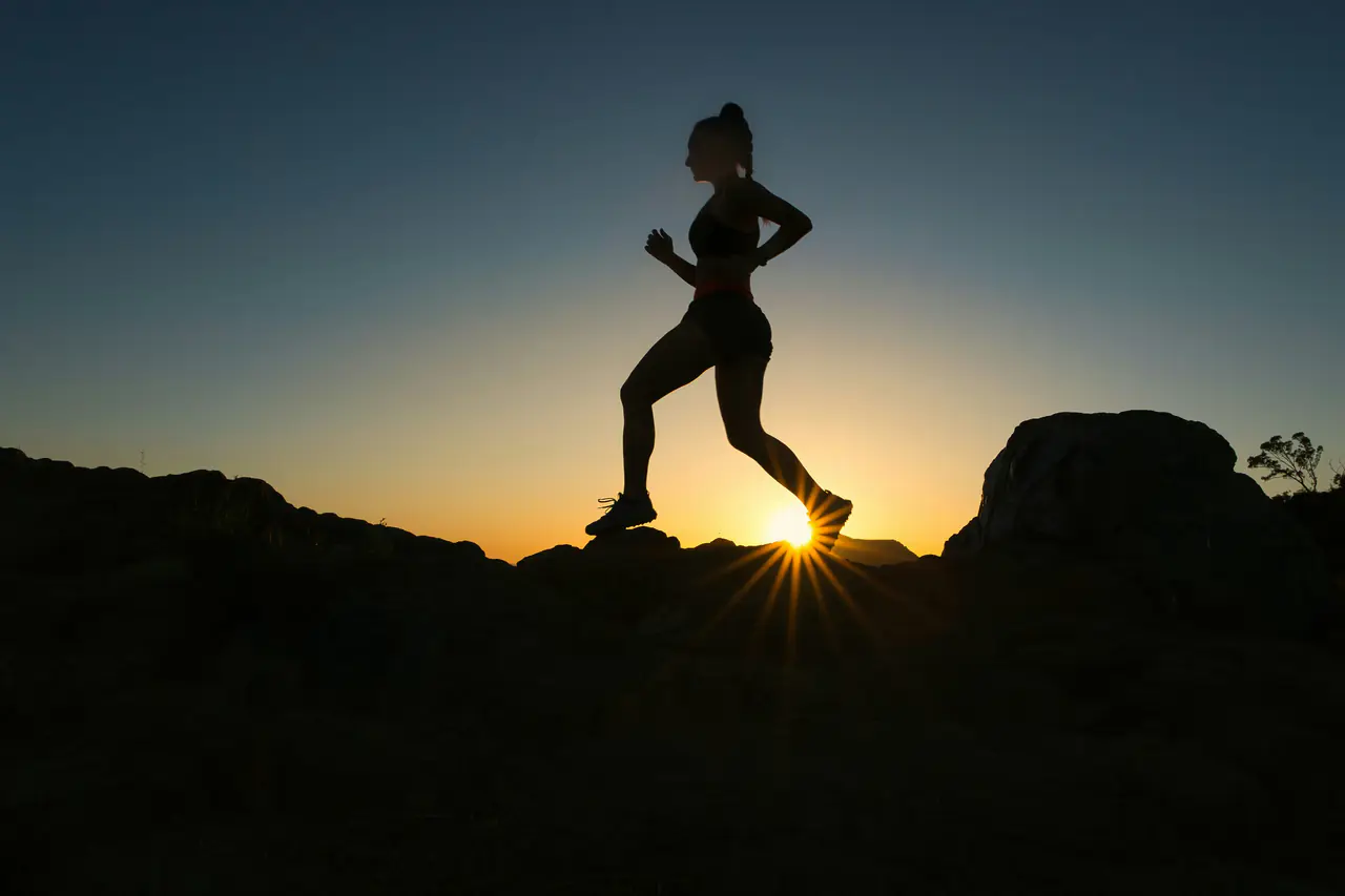 A trail runner silhouetted on a rocky ridge at sunset